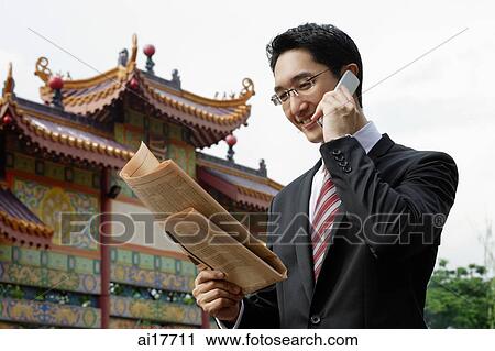 Businessman using mobile phone and reading newspaper View Large Photo Image Stock Image - Businessman using mobile phone and reading newspaper. Fotosearch