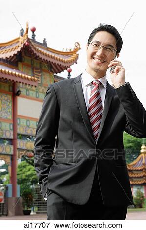 Businessman using mobile phone, standing in front of Chinese temple View Large Photo Image Stock Photo - Businessman using mobile phone, standing in front of Chinese temple. Fotosearch