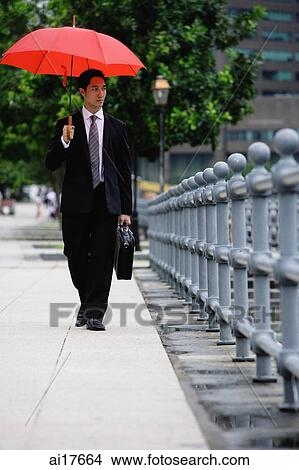 Businessman walking under red umbrella View Large Photo Image Picture - Businessman walking under red umbrella . Fotosearch