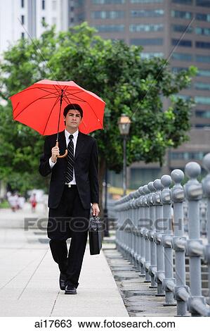 Stock Image - Businessman walking with briefcase and red umbrella. Fotosearch