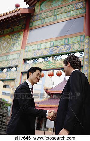Businessmen shaking hands, temple gate in the background View Large Photo Image Stock Photograph - Businessmen shaking hands, temple gate in the background . Fotosearch
