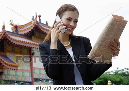 Businesswoman on mobile phone, looking at newspaper, Chinese temple in the background View Large Photo Image Stock Image - Businesswoman on mobile phone, looking at newspaper, Chinese temple in the background . Fotosearch
