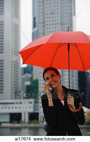 Businesswoman under red umbrella, using mobile phone View Large Photo Image Picture - Businesswoman under red umbrella, using mobile phone . Fotosearch