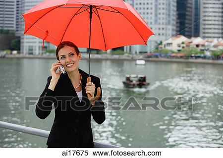 Businesswoman under red umbrella, using mobile phone, river in the background View Large Photo Image Stock Photography - Businesswoman under red umbrella, using mobile phone, river in the background . Fotosearch