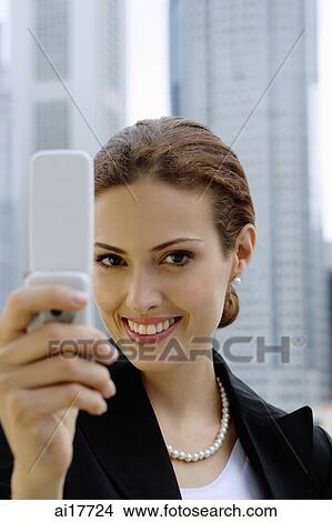 Businesswoman using mobile phone, photo messaging, looking at camera View Large Photo Image Picture - Businesswoman using mobile phone, photo messaging, looking at camera . Fotosearch