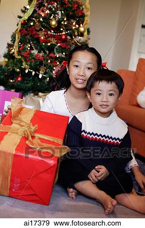 Stock Photo - Children sitting by Christmas tree, holding gift, portrait. Fotosearch
