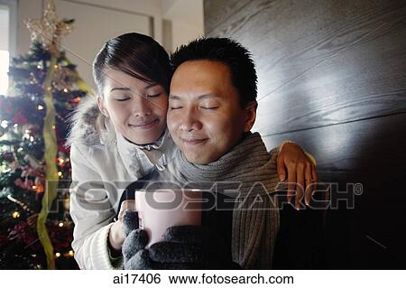Stock Photograph - Couple at home, dressed in winter wear, holding mug . Fotosearch