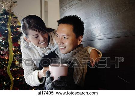 Couple at home, dressed in winter wear, woman passing mug to man View Large Photo Image Stock Photography - Couple at home, dressed in winter wear, woman passing mug to man . Fotosearch