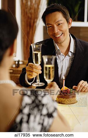 Stock Photography - Couple at table, toasting with champagne, cake on table . Fotosearch
