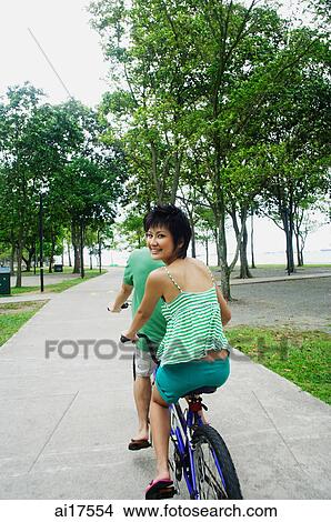Couple cycling on tandem bicycle, woman looking over shoulder View Large Photo Image Picture - Couple cycling on tandem bicycle, woman looking over shoulder. Fotosearch