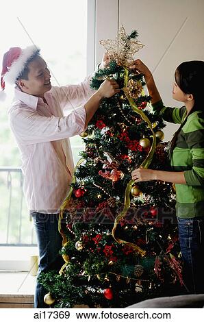 Stock Photo - Couple decorating Christmas tree at home . Fotosearch