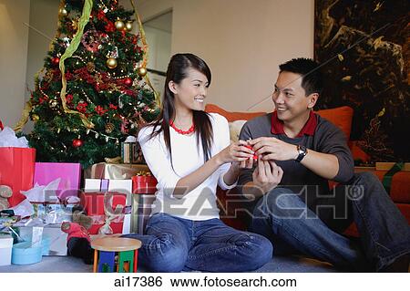 Couple giving each other Christmas gifts View Large Photo Image Stock Photograph - Couple giving each other Christmas gifts. Fotosearch