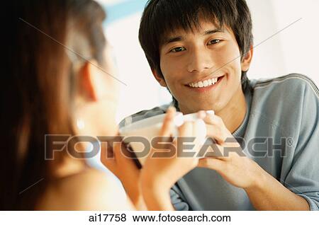 Stock Photo - Couple holding cups, man smiling at camera. Fotosearch