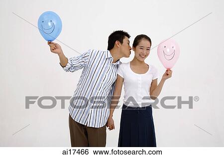 Couple holding hands, holding balloons, man leaning over to kiss woman on cheek View Large Photo Image Stock Photograph - Couple holding hands, holding balloons, man leaning over to kiss woman on cheek . Fotosearch