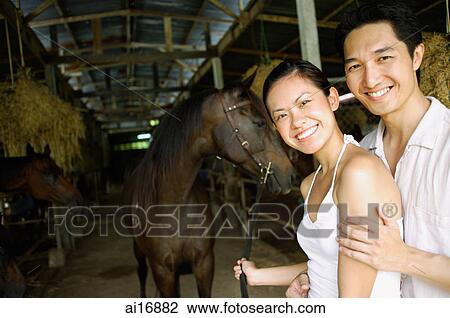 Couple in stable, standing with horse, looking at camera View Large Photo Image Stock Image - Couple in stable, standing with horse, looking at camera . Fotosearch