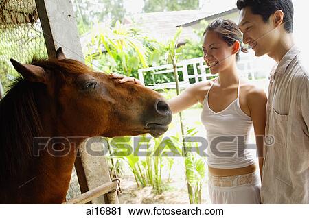 Stock Image - Couple in stable, woman petting horse . Fotosearch