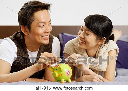 Couple lying on bed, putting coins in piggy bank View Large Photo Image Stock Photography - Couple lying on bed, putting coins in piggy bank . Fotosearch