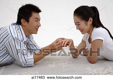 Couple lying on front, face to face, man holding womans ring finger View Large Photo Image Stock Image - Couple lying on front, face to face, man holding womans ring finger . Fotosearch