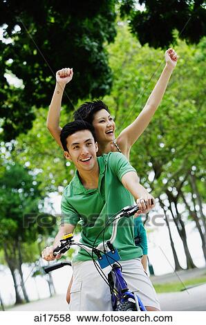 Stock Photo - Couple on tandem bicycle, woman raising arms in the air. Fotosearch