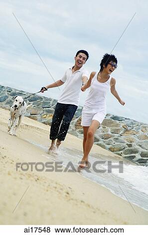 Stock Photo - Couple running on beach with dog . Fotosearch