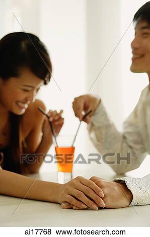 Couple sharing drink, sitting face to face, holding hands View Large Photo Image Stock Photo - Couple sharing drink, sitting face to face, holding hands . Fotosearch