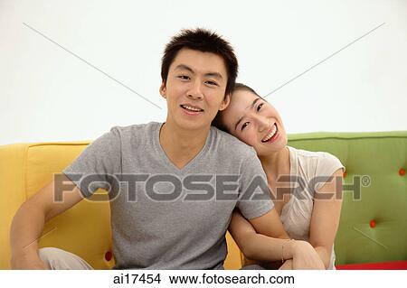 Couple sitting and facing camera, woman hugging mans arm View Large Photo Image Picture - Couple sitting and facing camera, woman hugging mans arm . Fotosearch