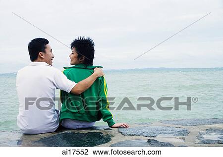 Couple sitting on breakwater, embracing, rear view View Large Photo Image Stock Image - Couple sitting on breakwater, embracing, rear view . Fotosearch