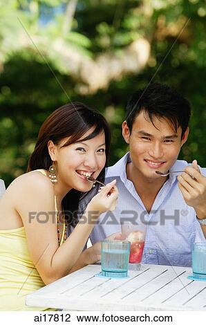 Couple sitting side by side, eating, smiling at camera View Large Photo Image Stock Image - Couple sitting side by side, eating, smiling at camera . Fotosearch