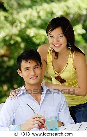 Couple smiling at camera, woman standing behind man, hand on shoulder View Large Photo Image Stock Image - Couple smiling at camera, woman standing behind man, hand on shoulder. Fotosearch
