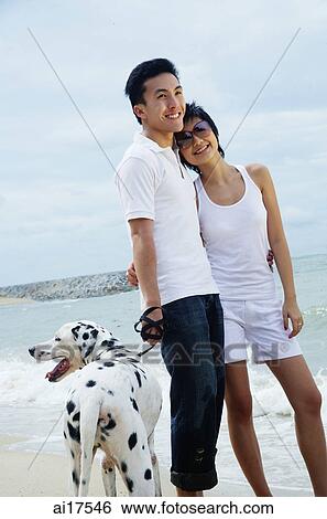 Stock Photograph - Couple standing on beach with Dalmatian . Fotosearch