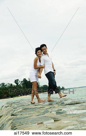 Stock Photo - Couple standing on breakwater, smiling at camera . Fotosearch