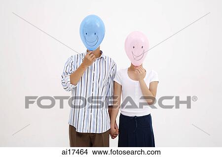 Couple standing side by side, holding hands, with balloons over their faces View Large Photo Image Picture - Couple standing side by side, holding hands, with balloons over their faces . Fotosearch