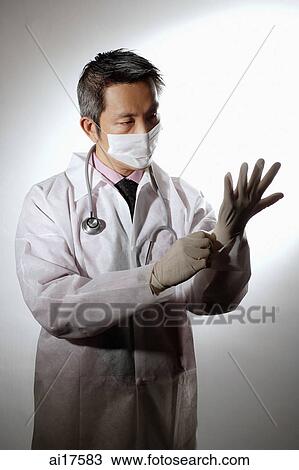 Stock Image - Doctor with face mask, putting on gloves . Fotosearch