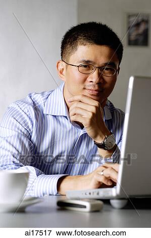 Executive using laptop, hand on chin, looking at camera View Large Photo Image Stock Photo - Executive using laptop, hand on chin, looking at camera. Fotosearch