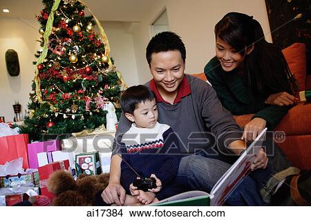 Family with one child, looking at book, Christmas tree behind them View Large Photo Image Picture - Family with one child, looking at book, Christmas tree behind them . Fotosearch
