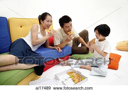 Stock Photo - Family with one child, sitting in living room, eating pizza . Fotosearch