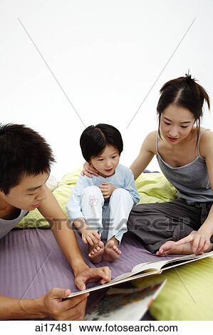 Family with one child sitting on bed, looking at book View Large Photo Image Stock Image - Family with one child sitting on bed, looking at book . Fotosearch