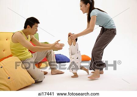 Father sitting on sofa, arms outstretched, toddler walking towards him, guided by the mother View Large Photo Image Stock Image - Father sitting on sofa, arms outstretched, toddler walking towards him, guided by the mother . Fotosearch