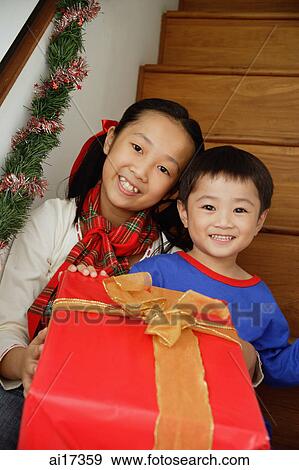 Stock Photo - Girl and boy sitting on stairs, holding present, smiling at camera . Fotosearch