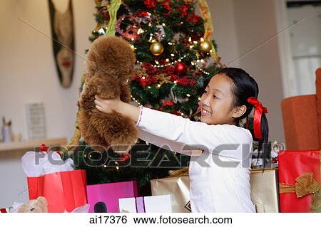 Stock Photograph - Girl sitting next to Christmas tree, holding stuffed toy . Fotosearch