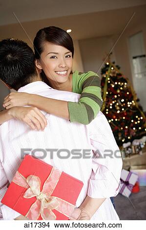 Man holding gift behind his back, woman embracing him View Large Photo Image Picture - Man holding gift behind his back, woman embracing him . Fotosearch