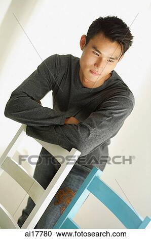 Stock Image - Man leaning arms on back of chair, looking away. Fotosearch
