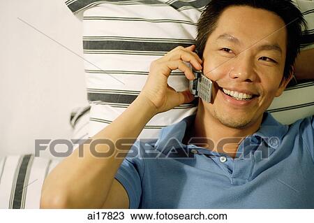 Man lying on bed, using mobile phone View Large Photo Image Stock Image - Man lying on bed, using mobile phone. Fotosearch