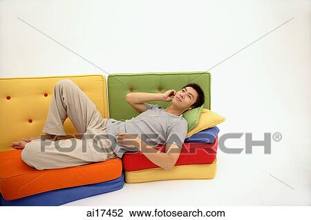 Man lying on multi-coloured sofa, listening to personal stereo View Large Photo Image Stock Image - Man lying on multi-coloured sofa, listening to personal stereo . Fotosearch