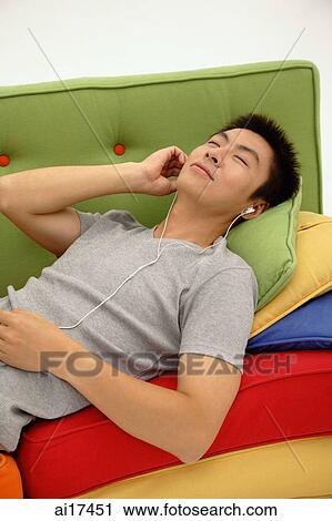 Stock Image - Man lying on sofa, listening to personal stereo . Fotosearch