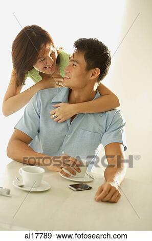 Man sitting at table, woman embracing him from behind View Large Photo Image Stock Photo - Man sitting at table, woman embracing him from behind. Fotosearch