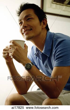Stock Photography - Man sitting, holding cup looking away. Fotosearch