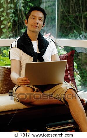 Stock Photo - Man sitting in living room, using laptop. Fotosearch