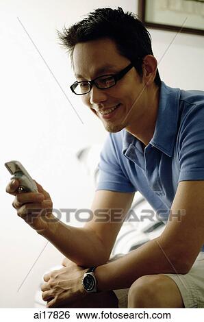 Man sitting, looking at mobile phone View Large Photo Image Stock Photograph - Man sitting, looking at mobile phone . Fotosearch