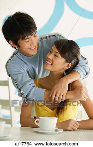 Man standing behind seated woman, embracing her from behind View Large Photo Image Picture - Man standing behind seated woman, embracing her from behind . Fotosearch